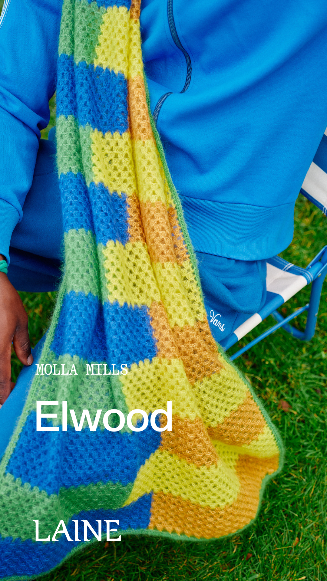 Colorful crocheted Elwood scarf with geometric pattern held by a person in blue clothing on grass.