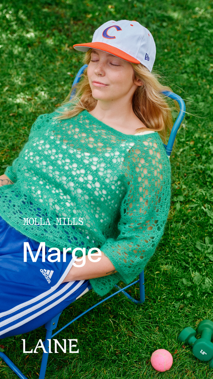 Woman wearing a green Marge sweater designed by Molla Mills and blue shorts sitting on a chair outdoors 
