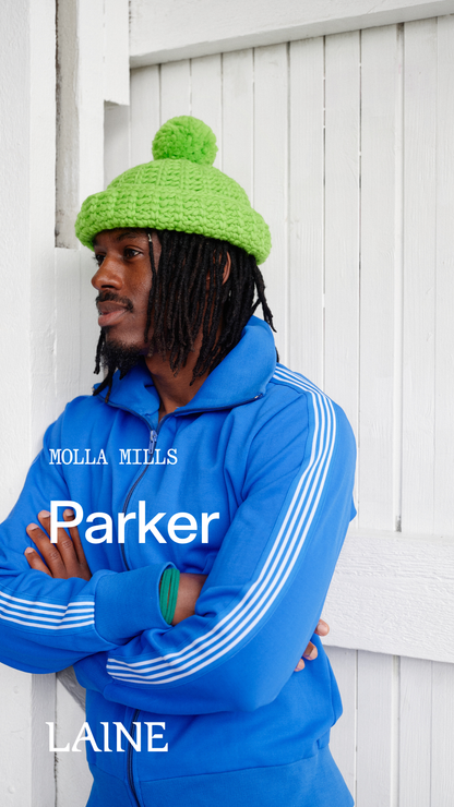 Person wearing a blue tracksuit with a Parker hat designed by Molla Mills against a white wooden background