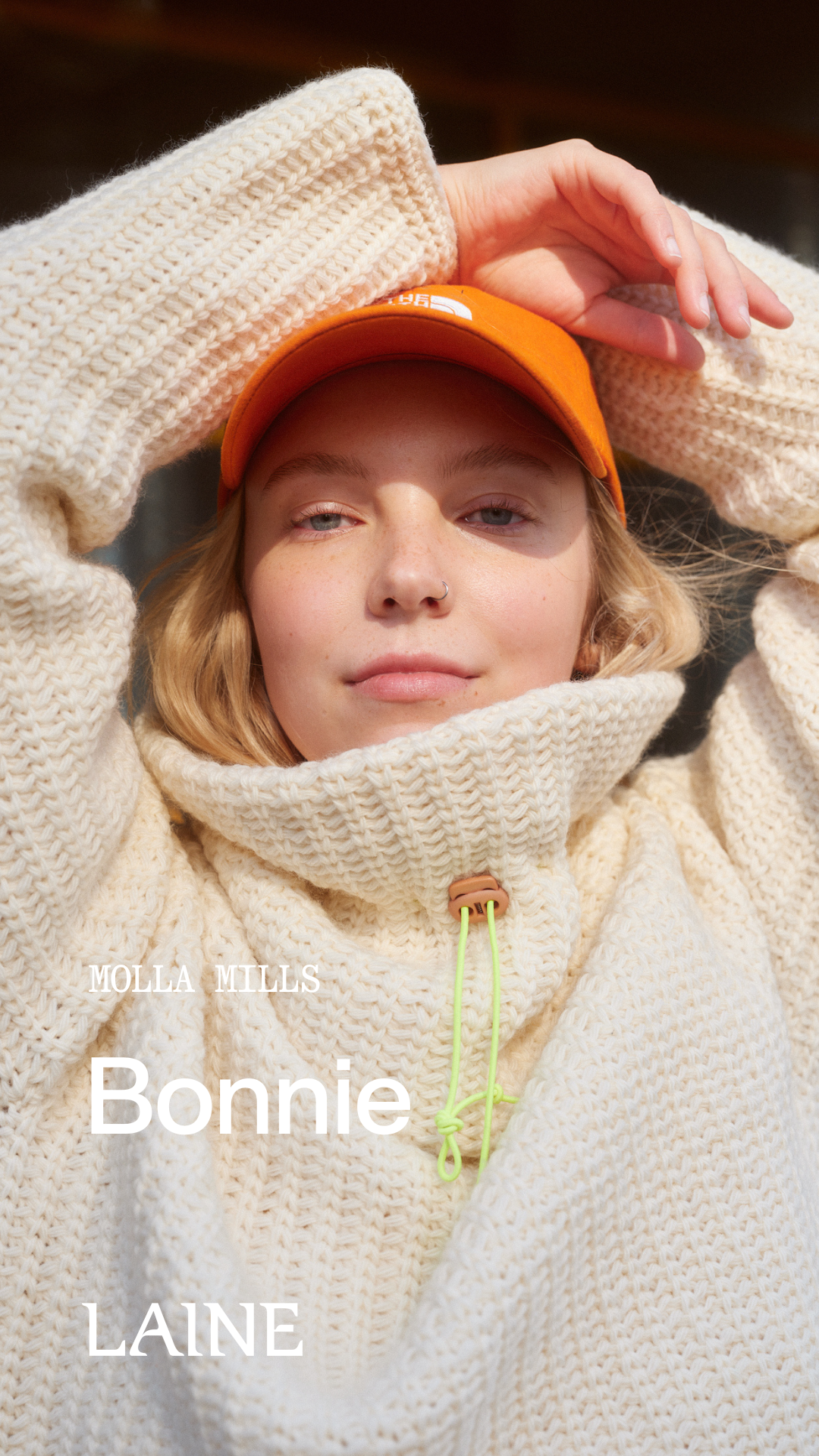 Person wearing a textured beige  Bonnie sweater designed by Molla Mills and orange cap with 'Bonnie' 