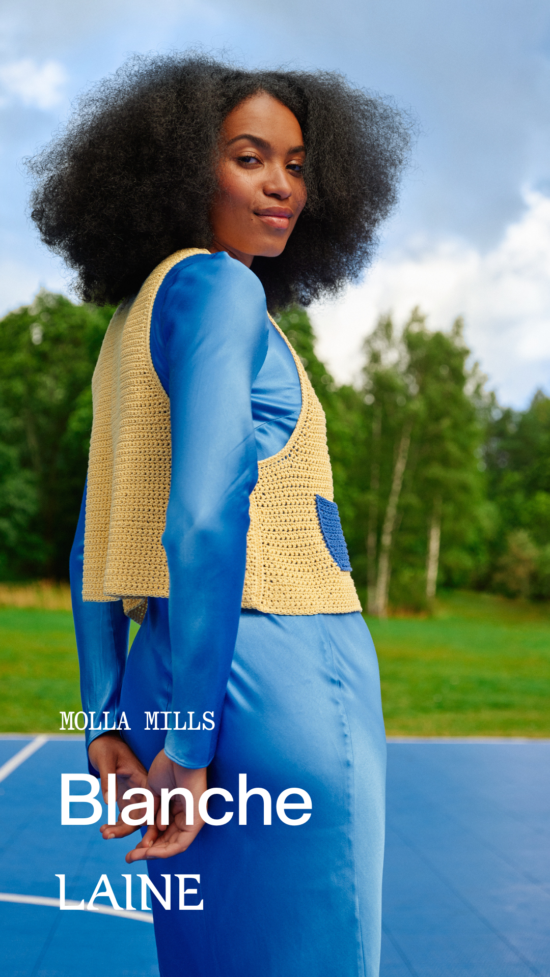 Woman wearing a blue dress with a beige Blanche crochet vest designed by Molla Mills outdoors