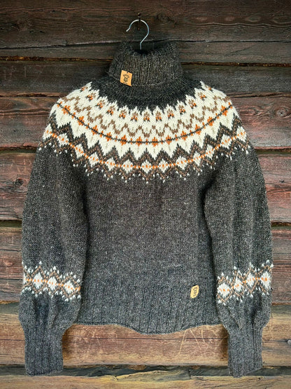A dark gray knit turtleneck sweater with a cream and orange stranded colorwork circular yoke pattern, hanging on a metal hanger against a rustic dark wood plank background.