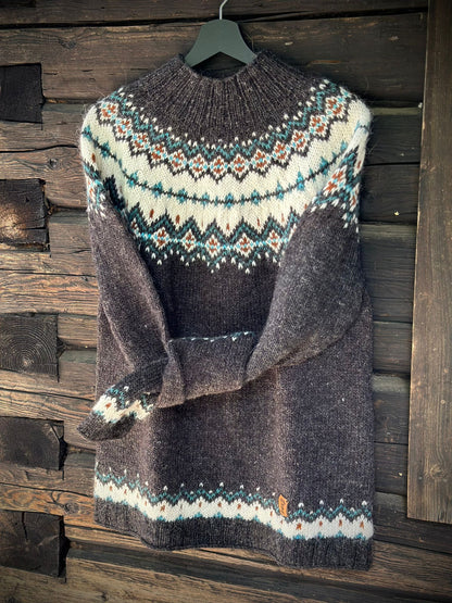 A dark gray knit sweater with a cream, teal, and orange stranded colorwork circular yoke pattern, hanging on a black hanger against a rustic dark wood plank wall.