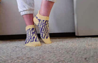 Person wearing yellow socks with blue patterns on a carpeted floor.